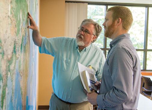 professor points to large map on wall while talking to student